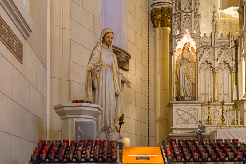 A picture of the front left of the Chapel of Loretto. You can see a statue of Mother Mary and candles lit below her. 